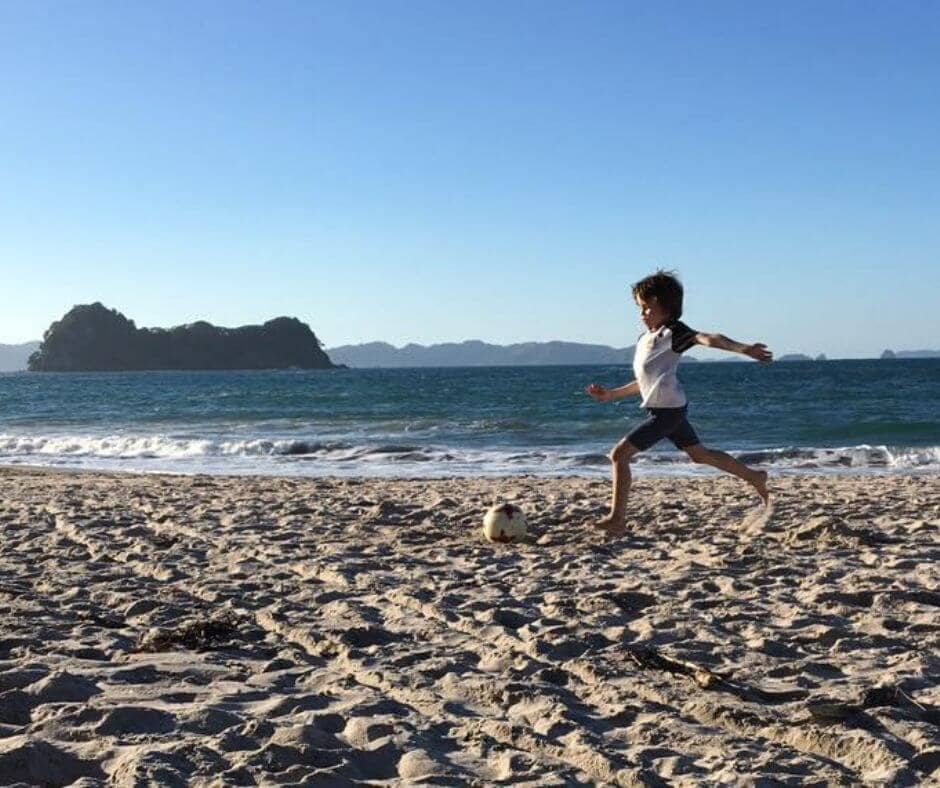 Lukas about to kick the ball on Hahei beach on a clear day