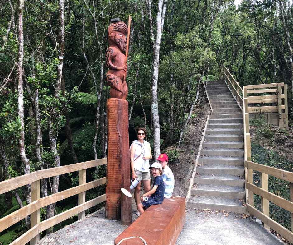 Family relax time next to the Pou Rākau at the Wairere Tapu Lookout. The Pou shows a figure holding a taiaha, måori weapon